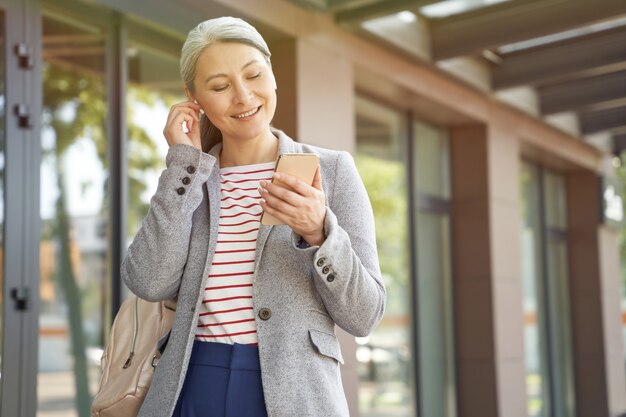 Portrait of attractive successful business woman adjusting wireless earphones and using her