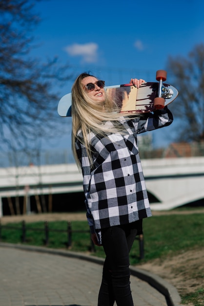 Portrait of attractive woman in sunglasses smiling standing with longboard