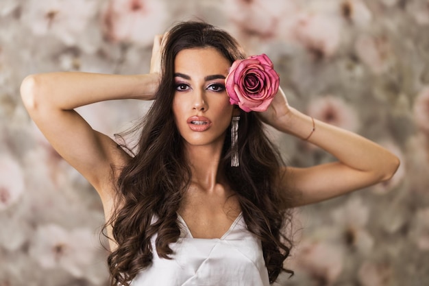 A portrait of an attractive woman with pink rose in her hair who is looking at camera