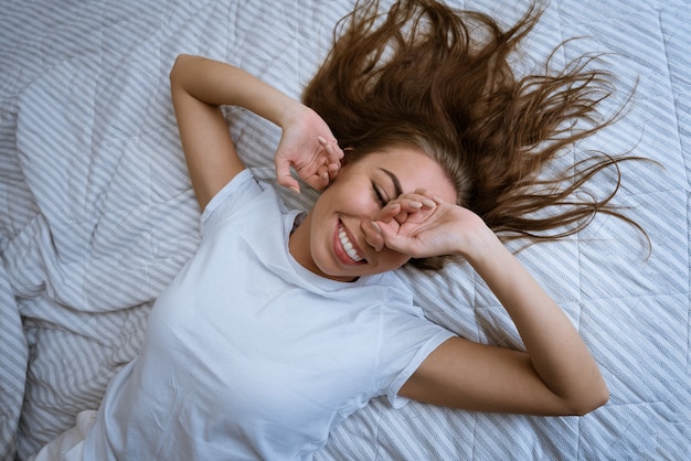 Portrait of an attractive young adult blonde woman in a white tshirt lying in bed with disheveled ha...