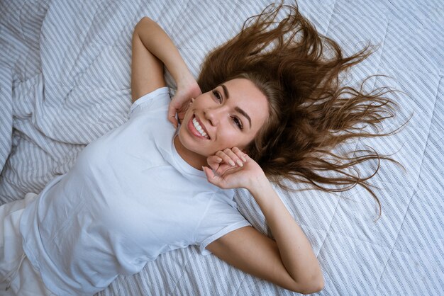 Portrait of an attractive young adult blonde woman in a white tshirt lying in bed with disheveled ha...