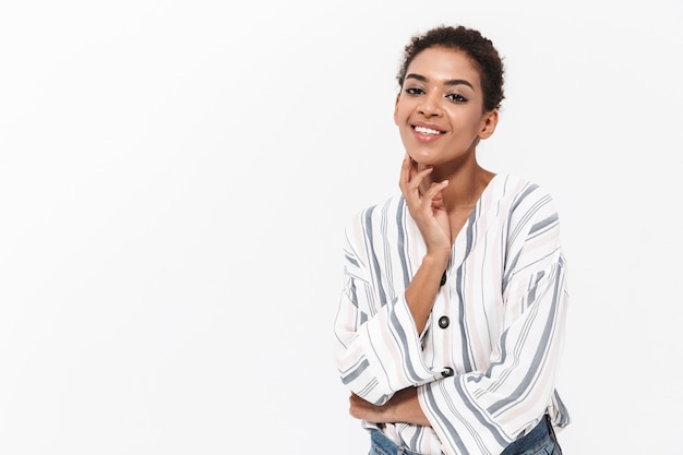 Portrait of an attractive young african woman standing isolated over white wall, touching face, posing