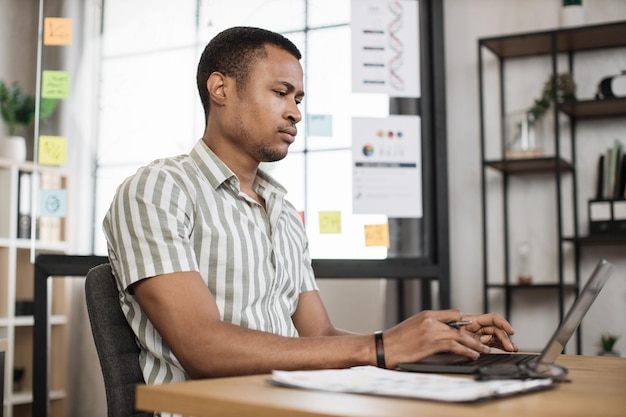 Portrait of attractive young businessman sitting at office desk and working with laptop