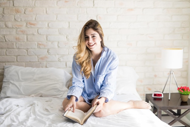 Portrait of an attractive young Caucasian woman in her pjs reading a book in the morning and smiling