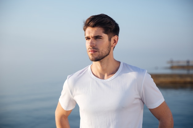 Portrait of attractive young man in white t-shirt standing near the sea