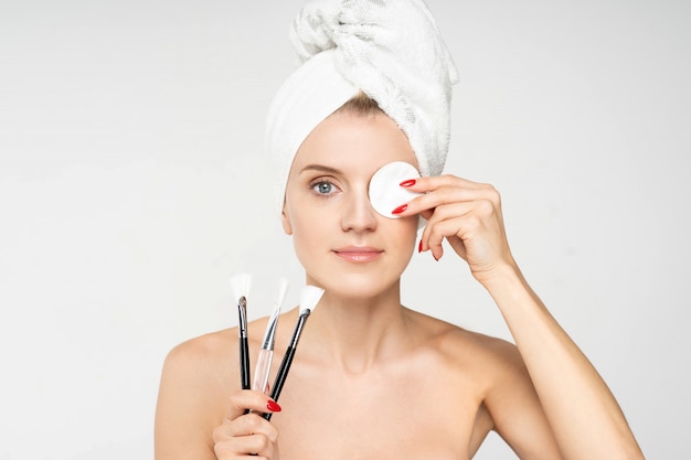 Portrait of an attractive young woman wearing bathroom towel on her head removing makeup with a cotton pad