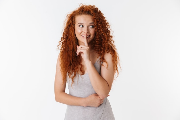 Portrait of an attractive young woman with long curly red hair standing isolated, showing silence gesture