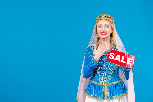 Portrait of azeri woman in traditional dress holding red sale nameplate on blue background novruz shopping ethnic