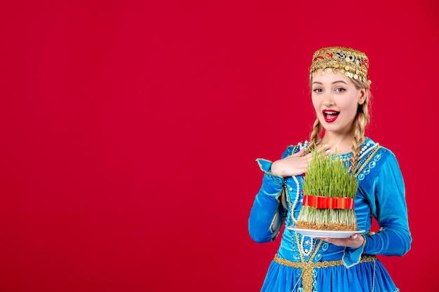 Portrait of azeri woman in traditional dress holding semeni studio shot on red background ethnic concept novruz