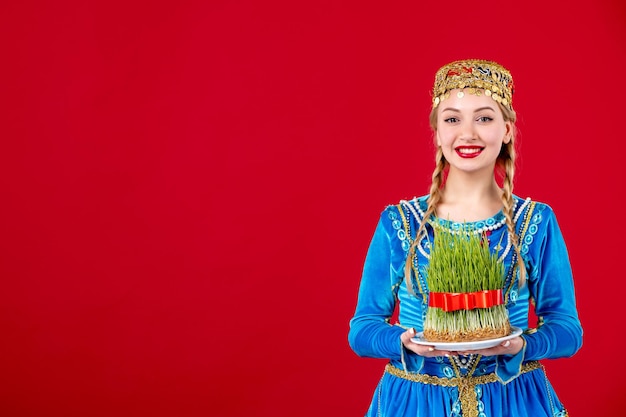 Portrait of azeri woman in traditional dress holding semeni studio shot on red background spring concept novruz