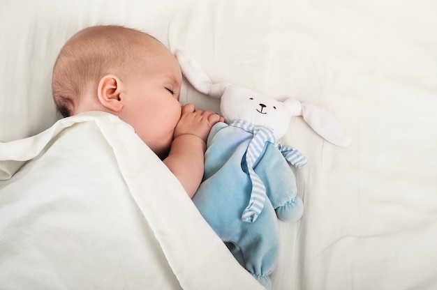 Portrait of baby 6 months sleeping with toy hare. Toddler, teething, baby sleep concept.