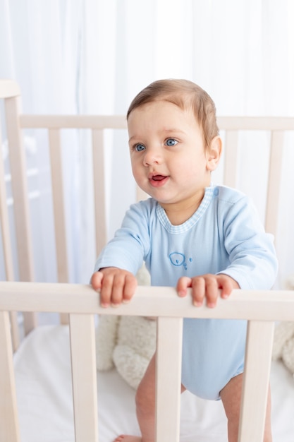 Portrait of a baby boy in a crib in a children's room with big blue eyes