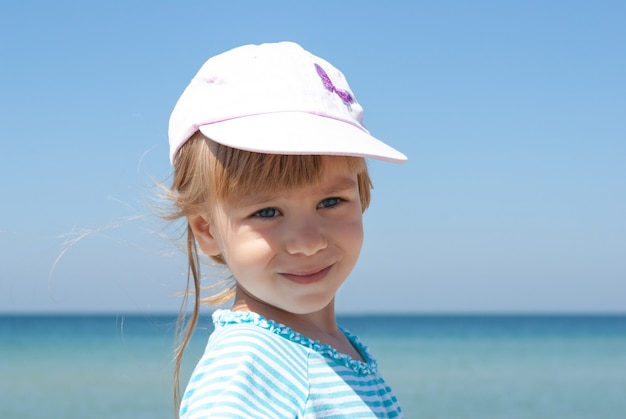 Portrait of a baby girl in a cap against the azure sea