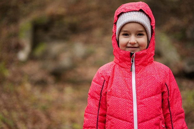 Portrait of baby girl in pink hooded jacket at autumn forest