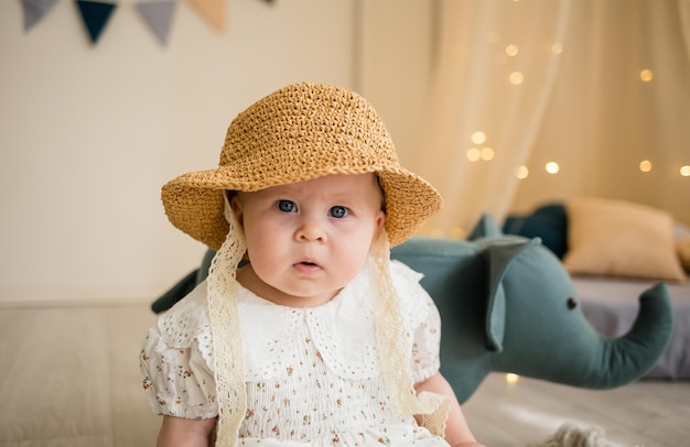 Portrait of a baby girl in a straw hat sitting in the nursery