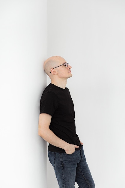 Portrait of a bald young man in a black tshirt with glasses on a gray background