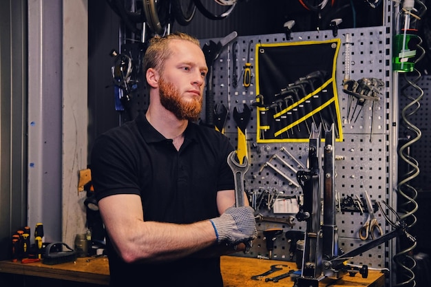 Portrait of bearded bicycle mechanic over tool stand background in a workshop.