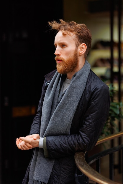 Portrait of a bearded brutal man leaning against the railing on the street