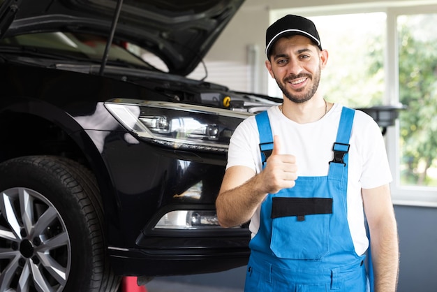 Portrait of bearded car mechanic in a car workshop shows thumbs up positive auto service worker