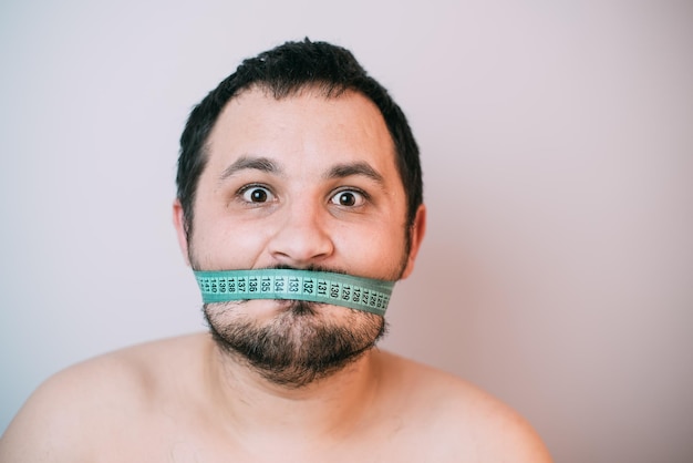 Portrait of bearded frustrated fat man with green measuring tape around his mouth healthy eating concept shooting in the Studio