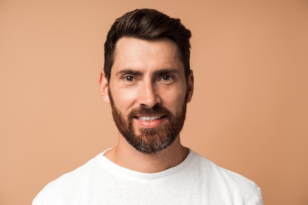 Portrait of bearded handsome man in casual style looking at the camera and smiling while posing Studio shot on beige background