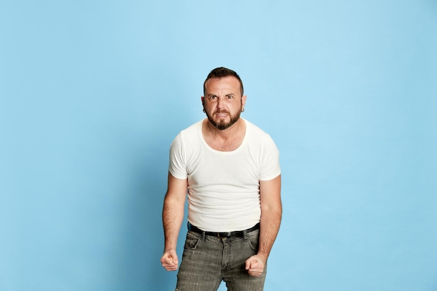 Portrait of bearded man in casual white tshirt showing anger and irritation holding fists clenched