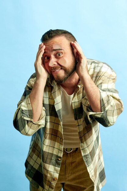 Portrait of bearded man in checkered shirt leaning on transparent glass against blue studio background Concept of human emotions lifestyle facial expression news sales Ad