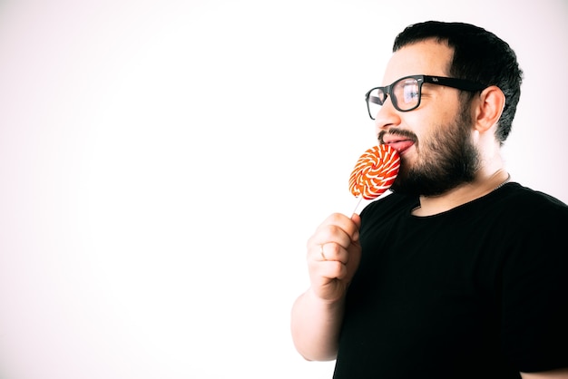 portrait of a bearded man wearing glasses with a big round red Lollipop