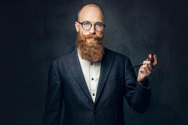 Portrait of bearded redhead English male smoking pipe over grey background.