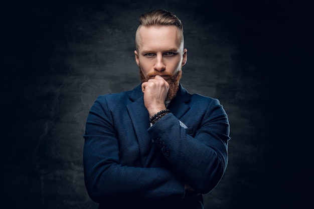 Portrait of bearded redhead hipster male dressed in a blue jacket over grey background.