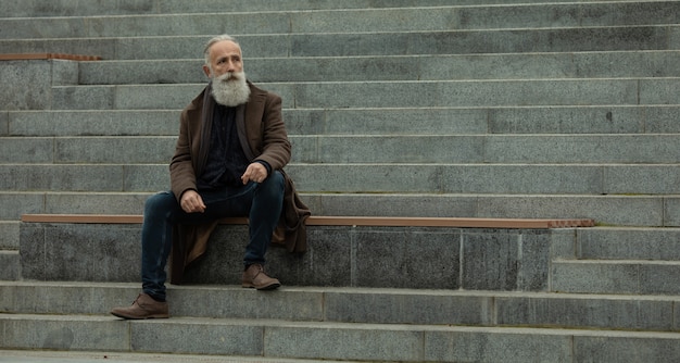 Portrait of a bearded senior man outdoors, sitting on a bench in a park.