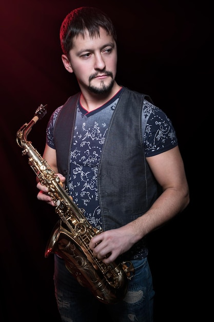 Portrait of a bearded young saxophonist with a golden saxophone isolated on a black background