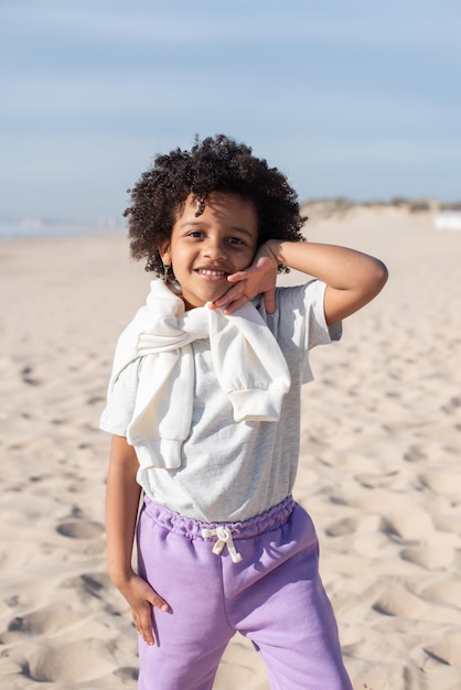 Portrait of beautiful African American girl on beach. Female model with curly hair in T-shirt and sweatpants posing. Portrait, beauty concept