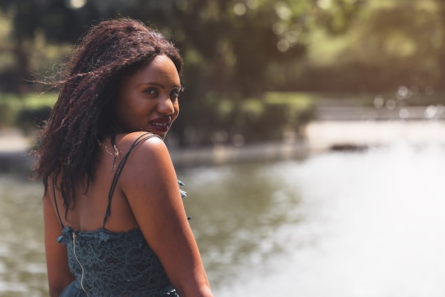 Portrait of beautiful african american woman smiling and looking away at park during sunset. Outdoor portrait of a smiling black girl. Happy cheerful girl laughing at park with colored hair band.
