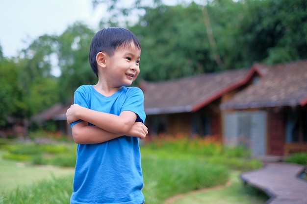 Portrait of a beautiful asian boy in the park, standing with arms crossed and smiling