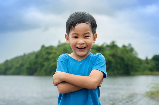 Portrait of a beautiful asian boy in the park, standing with arms crossed and smiling