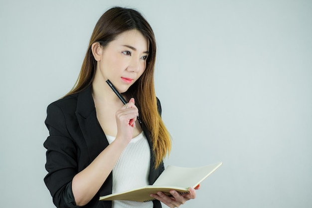 Portrait of beautiful asian business woman holding a notebook and thinking. Caucasian female model isolated on white background.