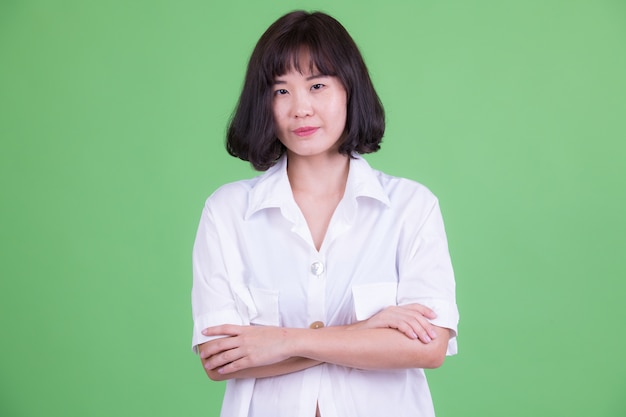 Portrait of beautiful Asian businesswoman with short hair against chroma key or green wall