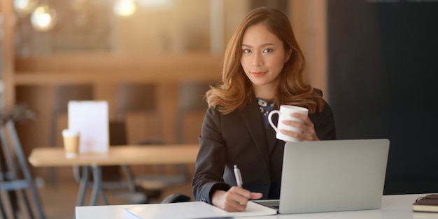 Portrait of beautiful asian businesswoman working on her project with laptop computer and drinking coffee