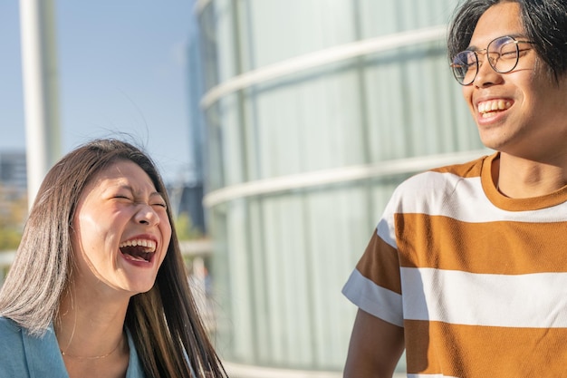 Portrait of a beautiful asian couple laughing outdoors in the student campus during a sunny day