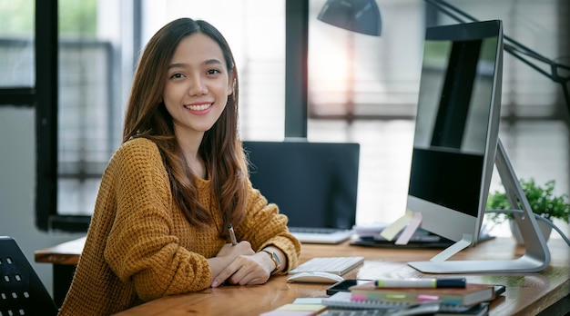 Portrait of Beautiful Asian freelancer Using Desktop Computer at home office Smiling and looking at camera