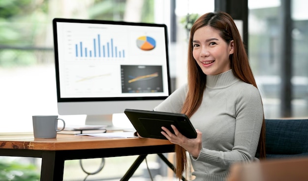 Portrait of Beautiful Asian freelancer Using tablet and Desktop Computer at home office Smiling and looking at camera