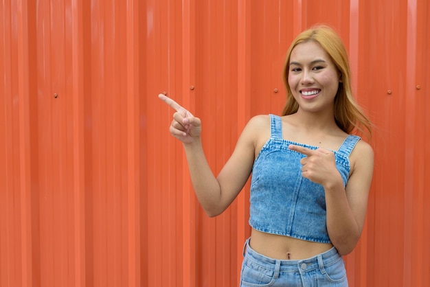 Portrait of beautiful Asian girl with blonde hair against orange background