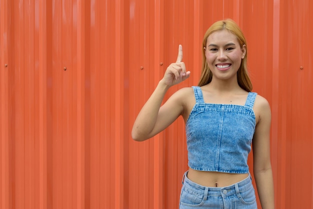 Portrait of beautiful Asian girl with blonde hair against orange background