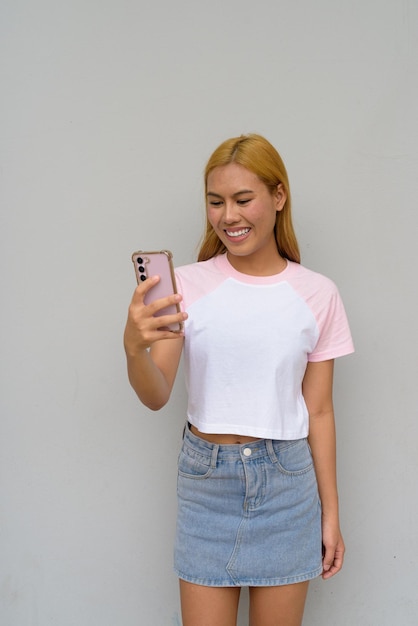 Portrait of beautiful Asian girl with blonde hair smiling against plain background