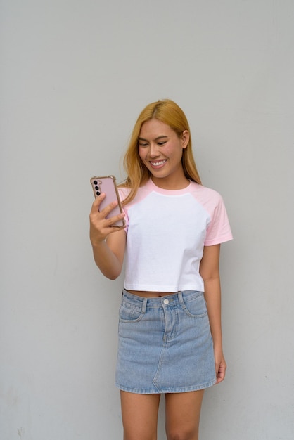 Portrait of beautiful Asian girl with blonde hair smiling against plain background