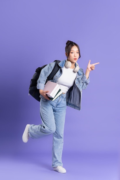 Portrait of a beautiful Asian schoolgirl wearing a backpack on a purple background