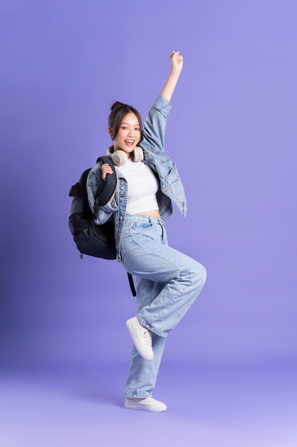 Portrait of a beautiful Asian schoolgirl wearing a backpack on a purple background