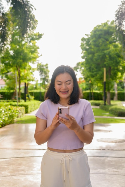 Portrait of beautiful Asian woman outdoor in park during summer using mobile phone