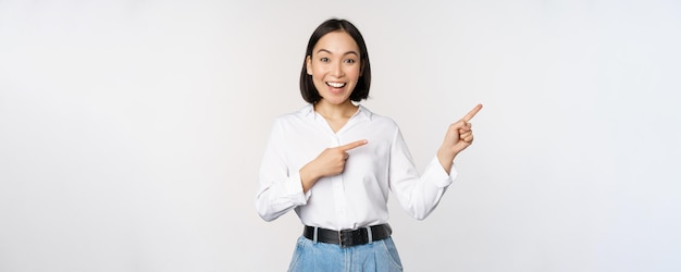 Portrait of beautiful asian woman saleswoman pointing fingers right and showing info banner or logo